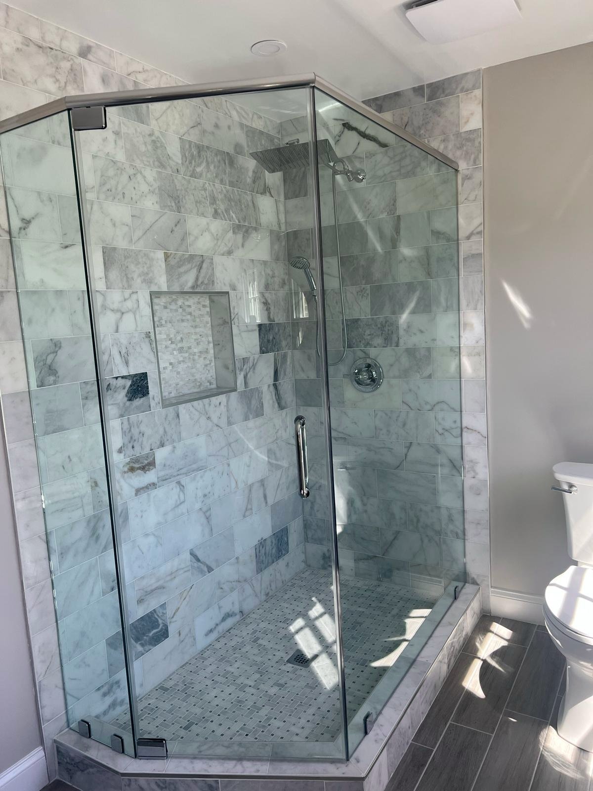 Finished glass-enclosed shower with marble-pattern tile.