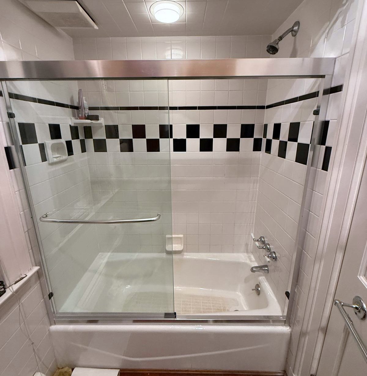 Sliding glass shower doors installed above a bathtub with black-and-white tile surround.