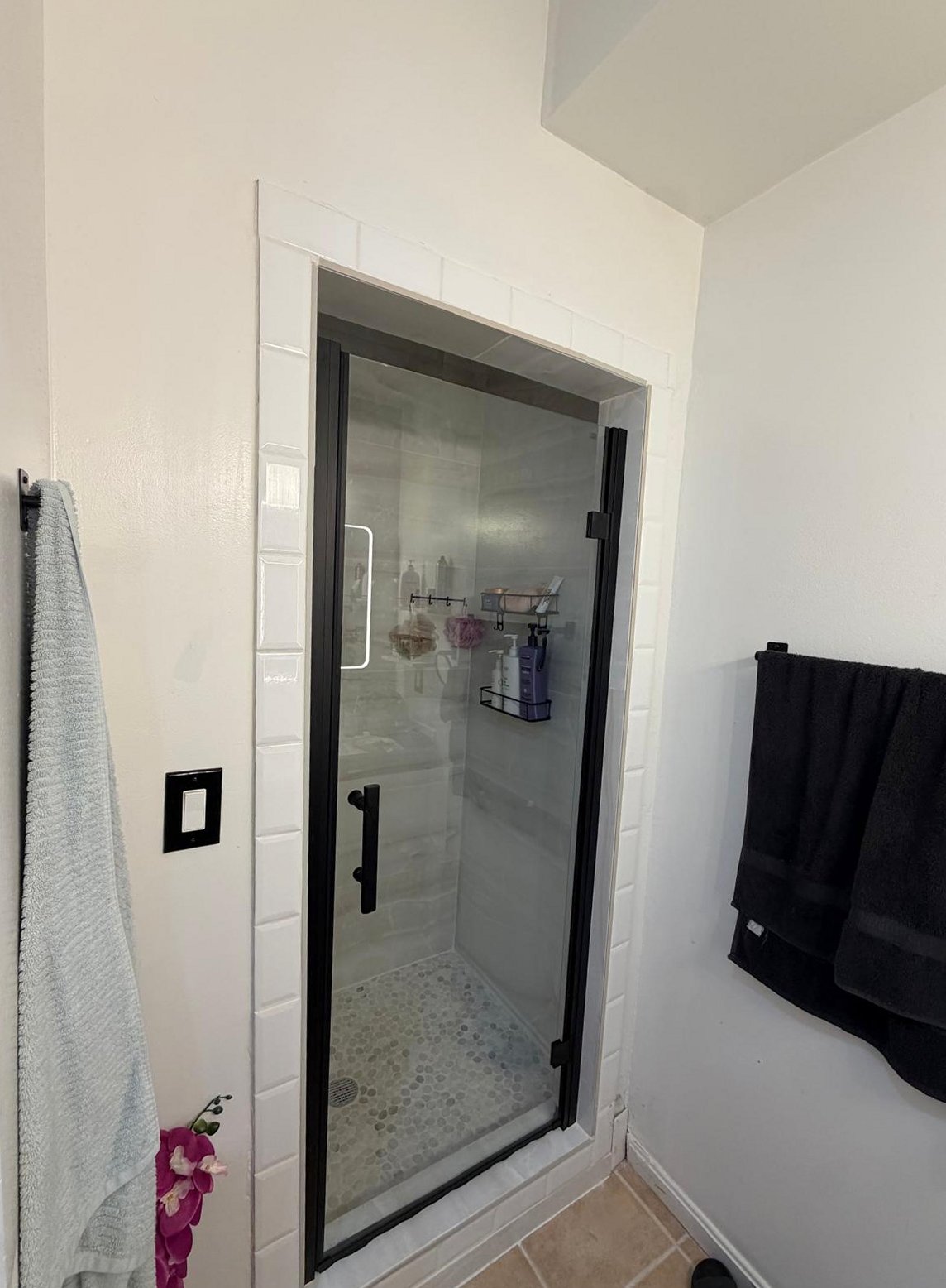 Renovated glass-enclosed shower with light marble-pattern tiles.