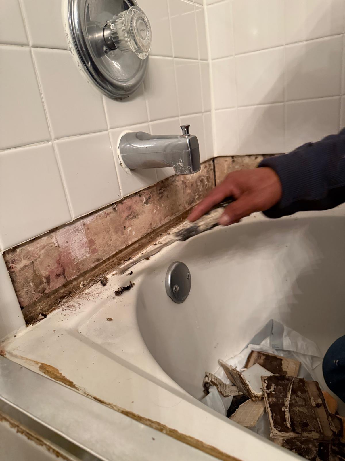 A strip of wall tiles removed above the bath to expose the area for repair.