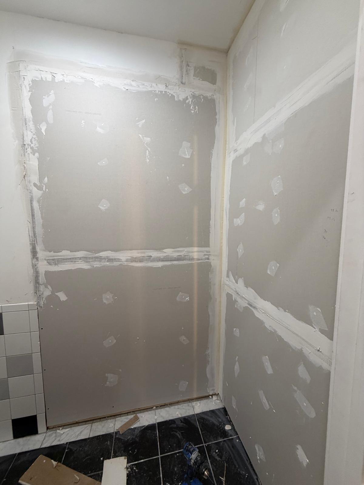 Closet walls with filled plasterboard joints above the existing dark tiled floor.