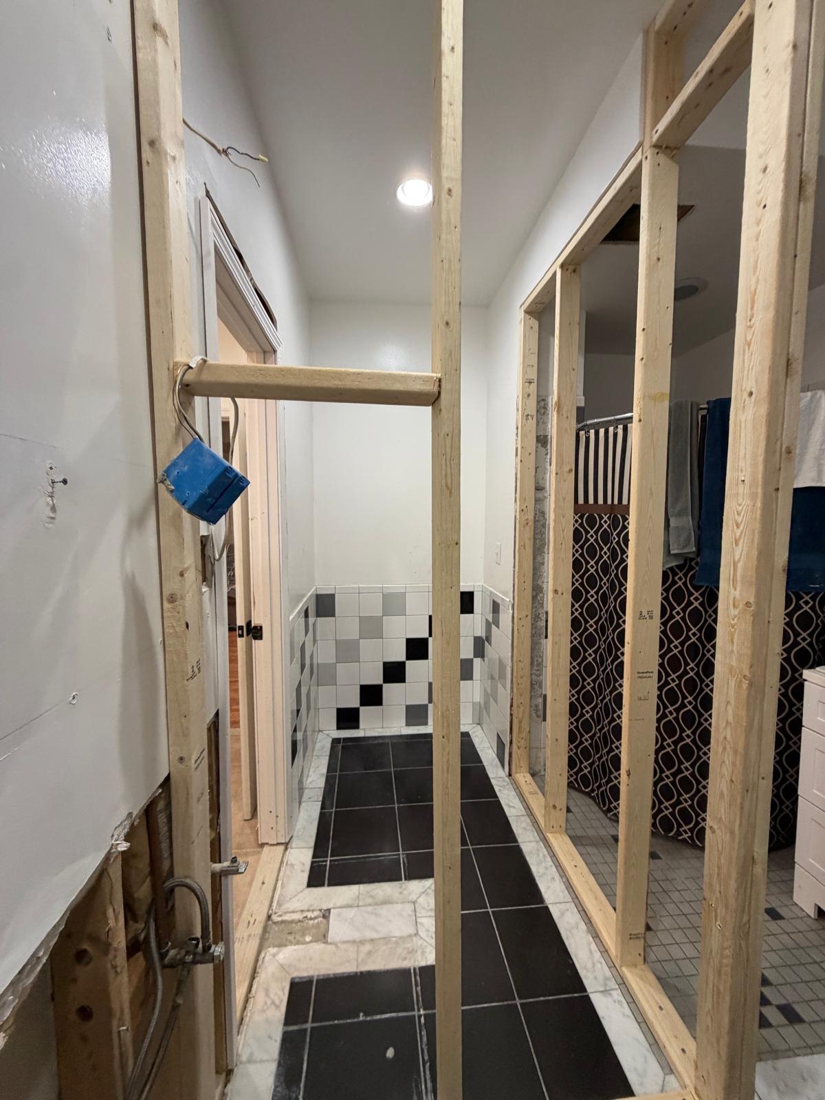 Exposed timber framing around the new closet with checkerboard wall tiles and dark floor tiles.