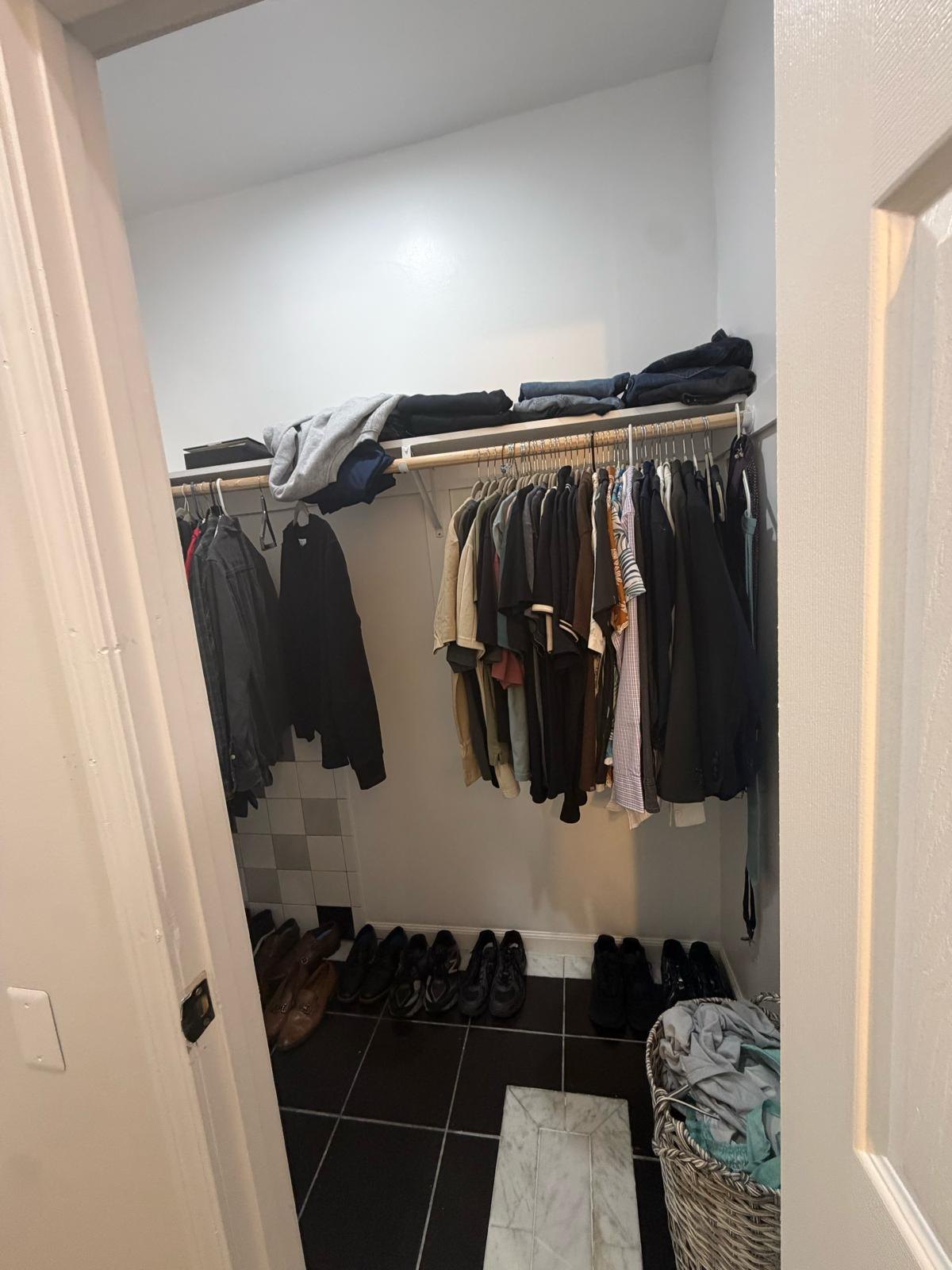 Fitted closet with painted walls, shelf, hanging rail and the retained checkerboard tiles.