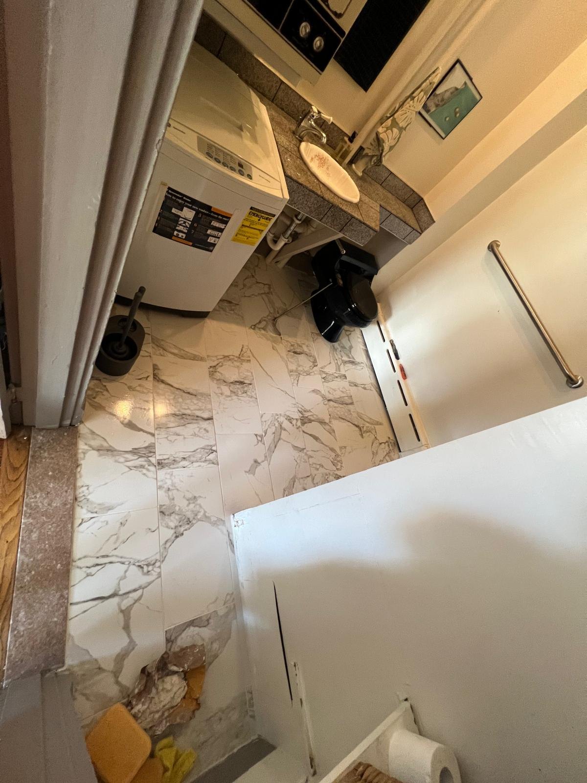 Marble-pattern floor tiles laid around the vanity and toilet, with doorway finishing still in progress.