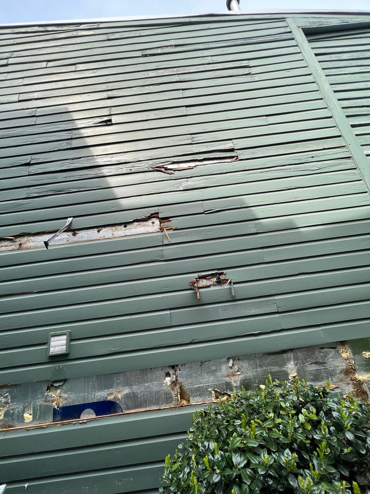 Weathered green siding with damaged timber and exposed patches.