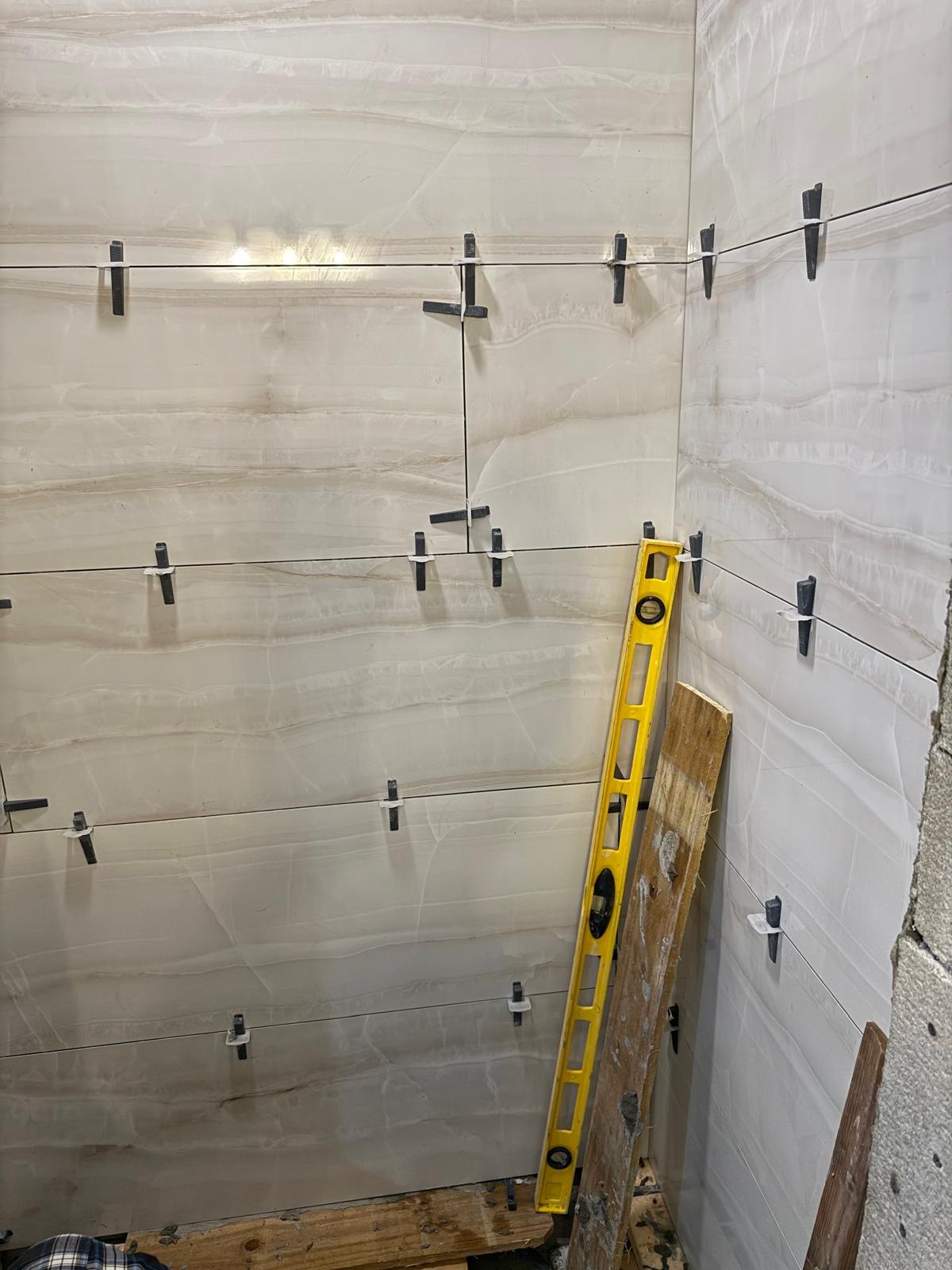 Light marble-pattern wall tiles being installed with levelling clips.